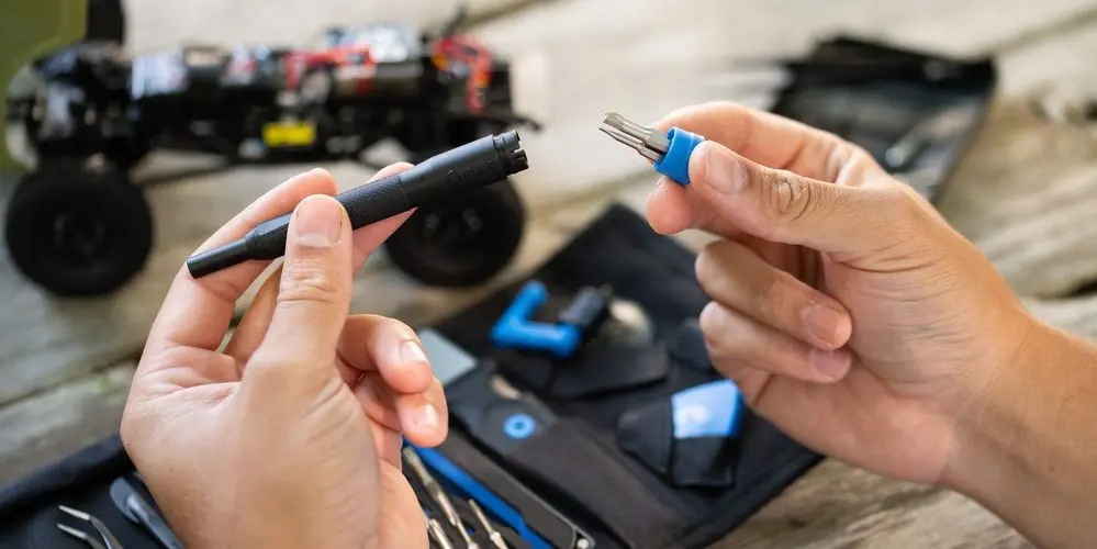 Des mains tiennent des outils près d'une voiture jouet et d'outils. Une trousse à outils noire est au premier plan.