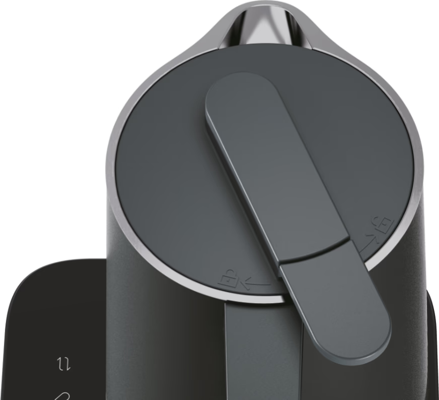 Bollitore nero con coperchio grigio scuro e manico. Il coperchio ha un simbolo di blocco/sblocco.