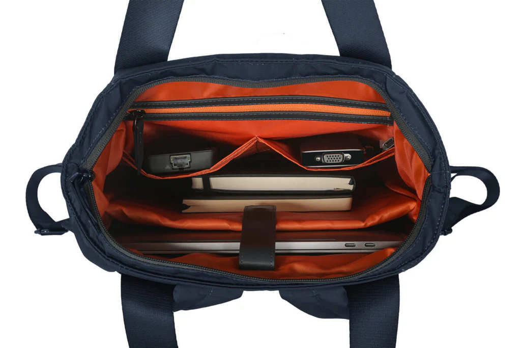 Bolso tote azul marino abierto con interior naranja, portátil y accesorios.