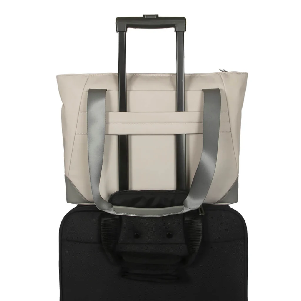 Bolso tote beige encima de una maleta negra. La bolsa tiene asas grises. Se ve un asa de la maleta.