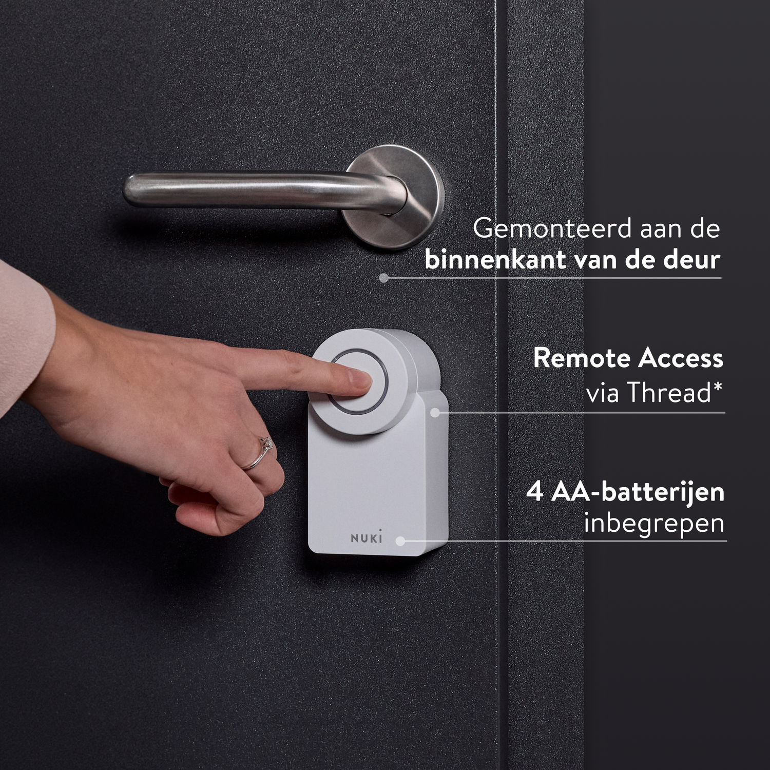 Hand drukt op witte Nuki smart lock knop op zwarte deur. Zilveren handvat erboven. Tekst: Remote Access, 4 AA batterijen.
