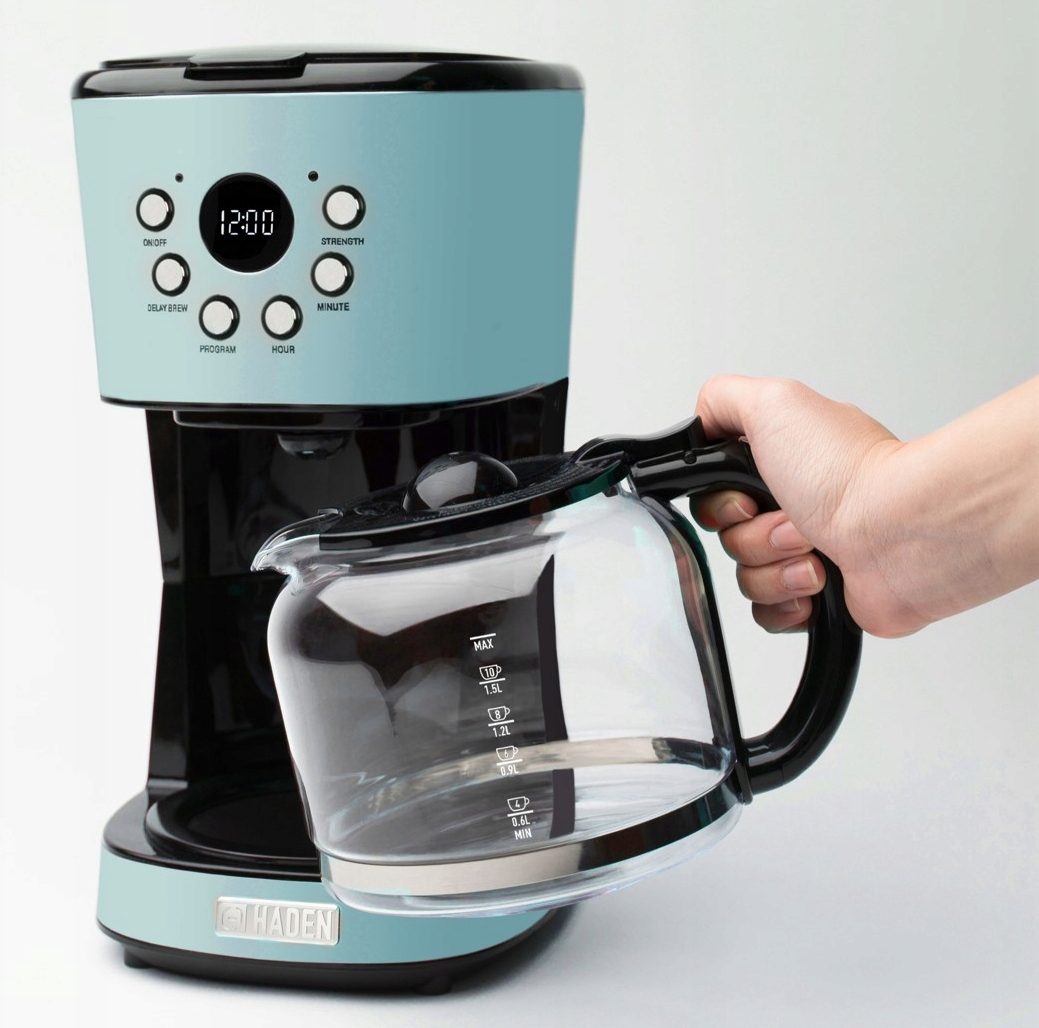 Osoba trzymająca szklany dzbanek obok niebiesko-czarnego ekspresu do kawy.