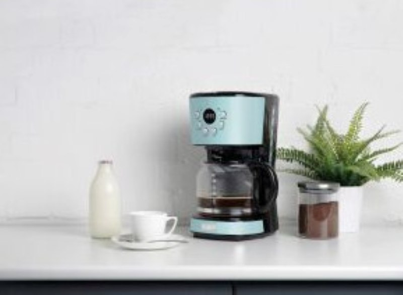 Niebiesko-czarny ekspres do kawy z butelką mleka, filiżanką i rośliną na białym blacie.