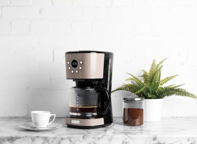 Beżowo-czarny ekspres do kawy z kawą, filiżanką i rośliną na marmurowym blacie na tle ceglanej ściany.