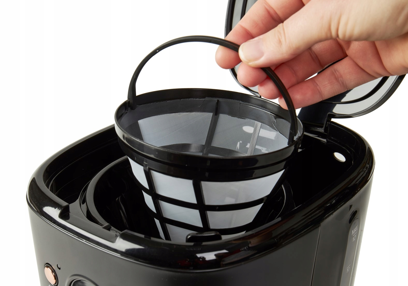 Ręka wyjmująca kosz filtra z czarnego ekspresu do kawy, pokazująca filtr.
