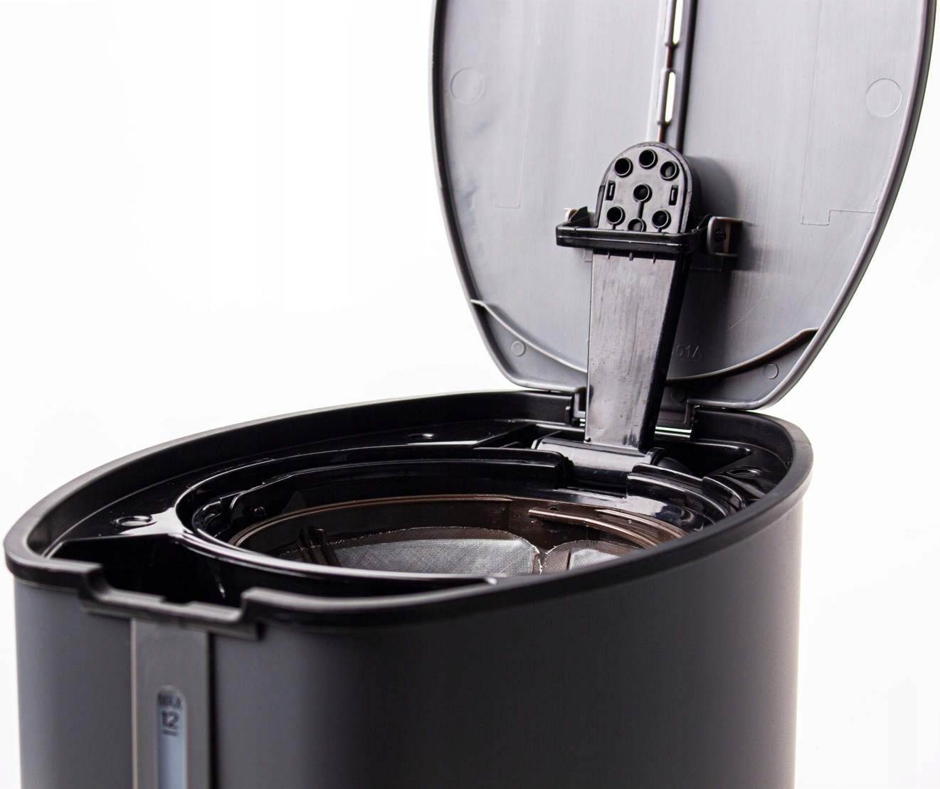 Zbliżenie otwartej pokrywy czarnego ekspresu do kawy, odsłaniające komorę filtra.