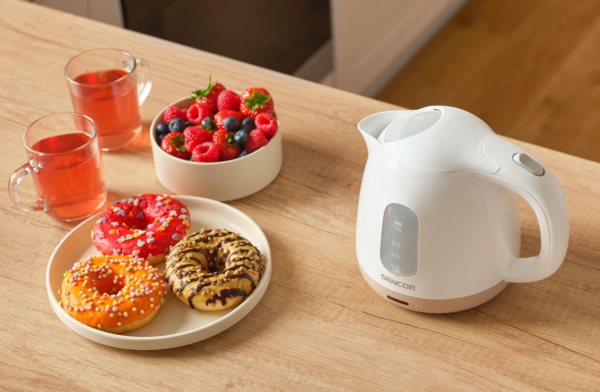 Czajnik elektryczny na stole z pączkami, jagodami i napojami.