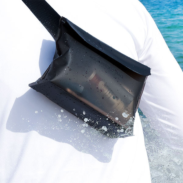 Czarna, wodoodporna torba na ramieniu osoby. Krople wody są na torbie. Tłem jest ocean.