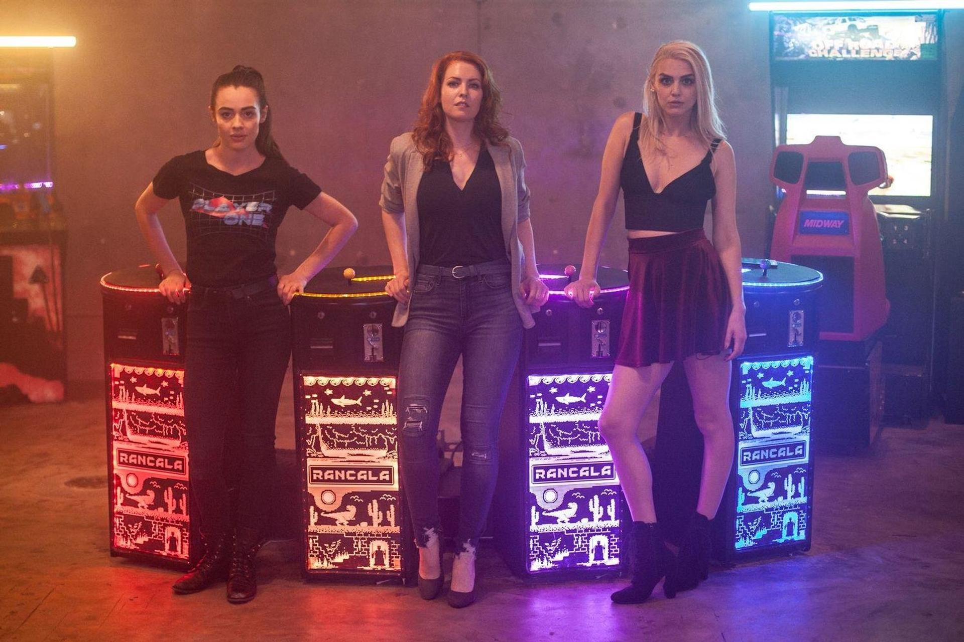 Drei Frauen stehen in einer Spielhalle. Zwei stehen in der Nähe von Spielautomaten.