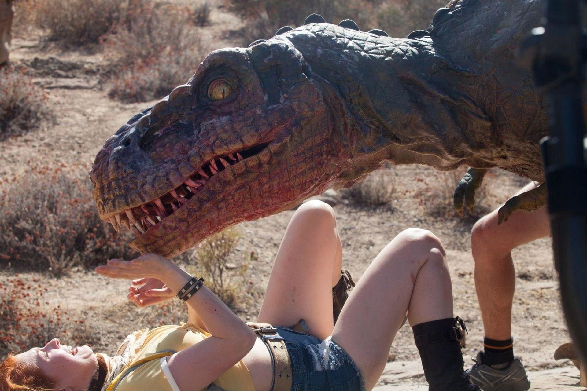 Eine Frau liegt am Boden in der Nähe einer Dinosaurier-Requisite. Eine Person steht in der Nähe.