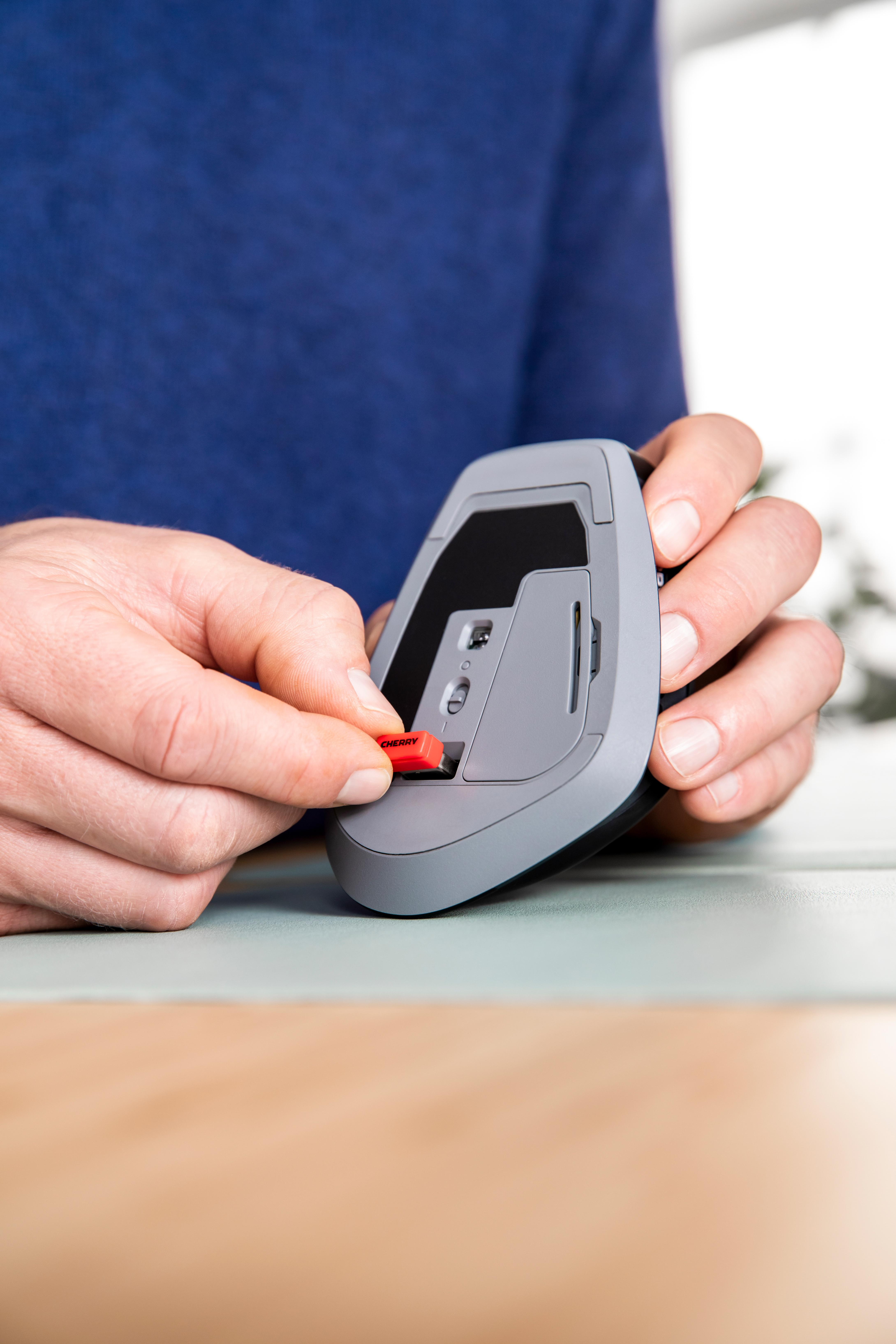 Hände stecken einen roten "CHERRY" USB-Empfänger in eine graue Computermaus.