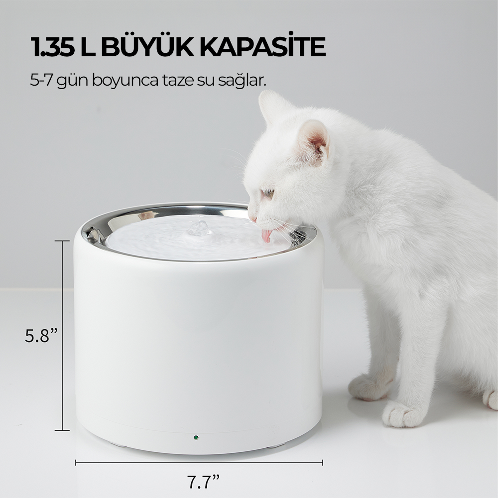 Beyaz bir kedi beyaz bir su çeşmesinden içiyor. Çeşmenin gümüş rengi üst kısmı var ve boyutları belirtilmiş.