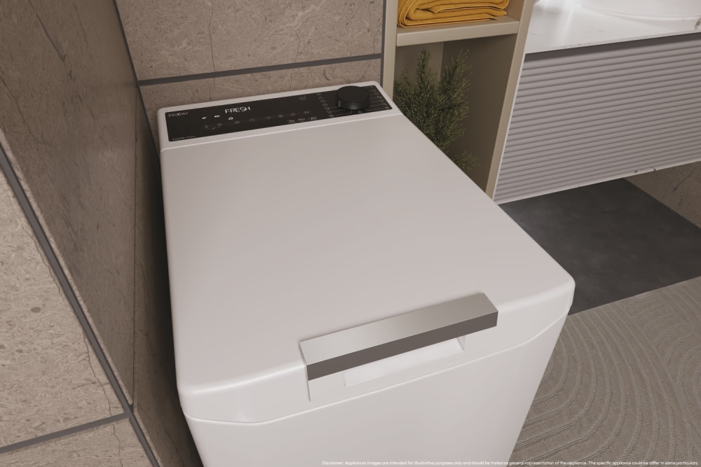 Eine weiße Waschmaschine mit silbernem Griff in einem Badezimmer. Beigefarbene Wand und Regal mit Handtüchern im Hintergrund.
