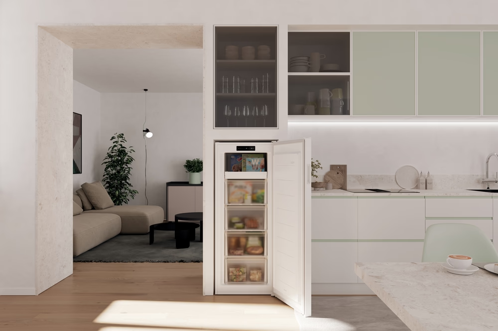 Innenaufnahme: Offener Gefrierschrank, moderne Küche, Wohnzimmer sichtbar. Beiges Sofa, Pflanze, schwarze Tische, mintgrüne Schränke, Kaffeetasse.