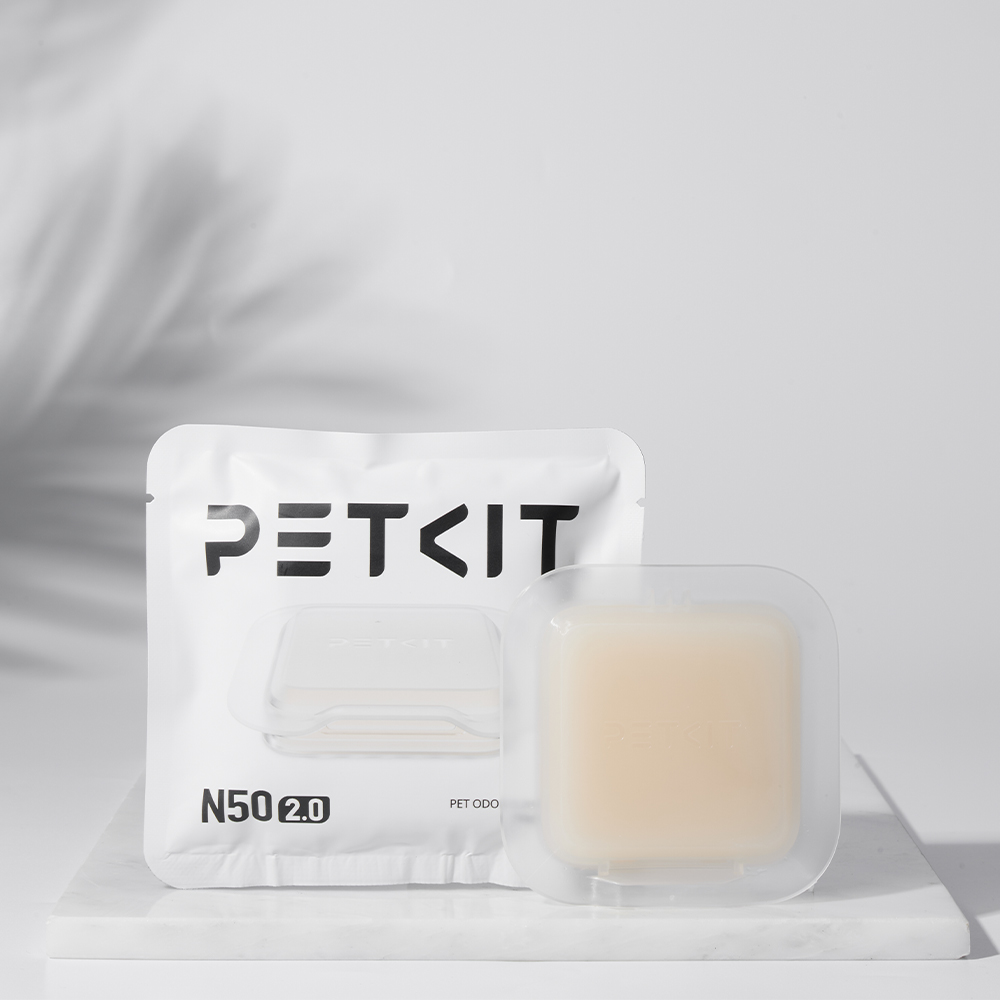 Beyaz PETKIT paketi ve şeffaf kare ped beyaz mermer yüzeyde. Arka planda yaprak gölgeleri görülüyor.