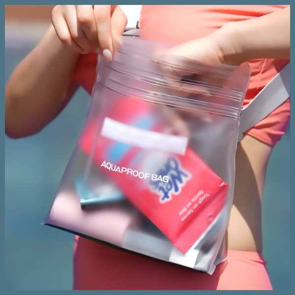 Kobieta otwiera przezroczystą, wodoodporną torbę. W środku widoczny jest czerwony pakiet Wet Ones i inne przedmioty. Ma na sobie kostium kąpielowy.