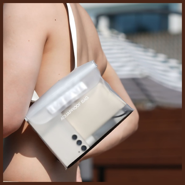 Osoba w białym stroju kąpielowym trzyma przezroczystą, wodoodporną torbę. Torba zawiera telefon. Tło jest słoneczne.