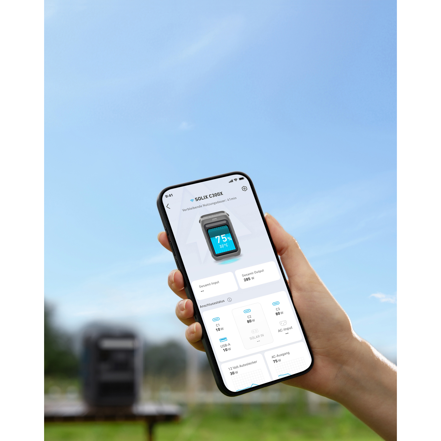 Une main tenant un téléphone affichant des statistiques de batterie. L'écran montre l'entrée, la sortie et le pourcentage de batterie. Ciel bleu en arrière-plan.