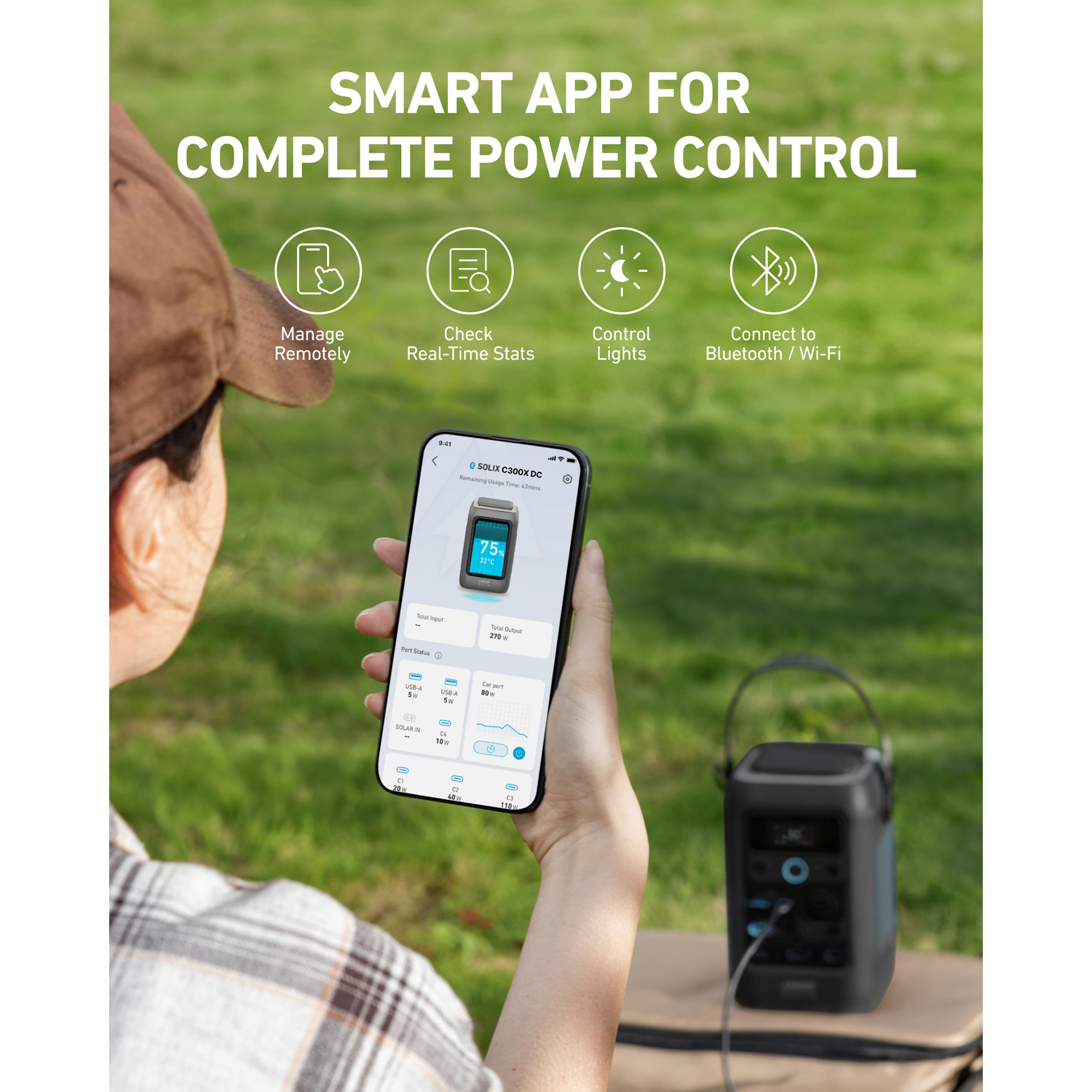 A person holding a phone displaying power stats, with a power station in the background, outdoors on grass.