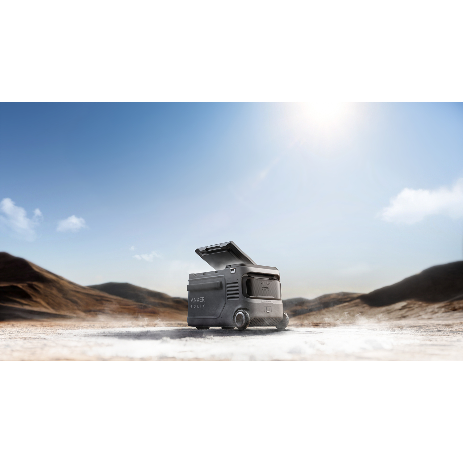 Anker Solix cooler on a desert-like landscape. Open lid, gray color, blue sky with clouds and sun. Rolling wheels.