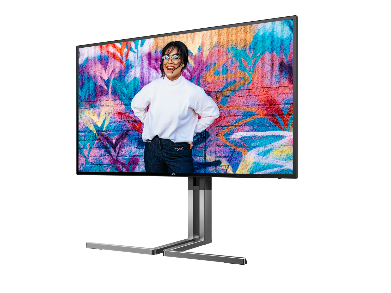 Un monitor muestra a una mujer sonriendo, de pie frente a un graffiti. Lleva un suéter blanco y jeans. El monitor está sobre un soporte.