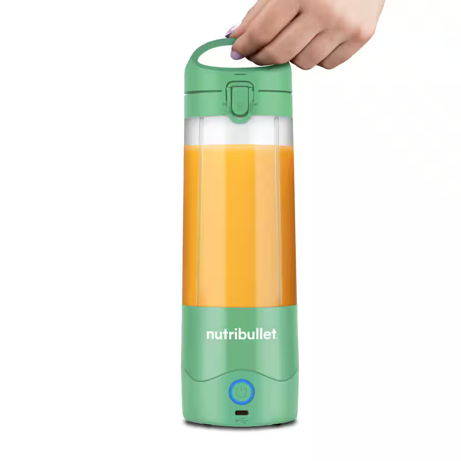 Ręka trzyma zielony Nutribullet z pomarańczowym płynem w środku. Podstawa ma przycisk zasilania. Białe tło.