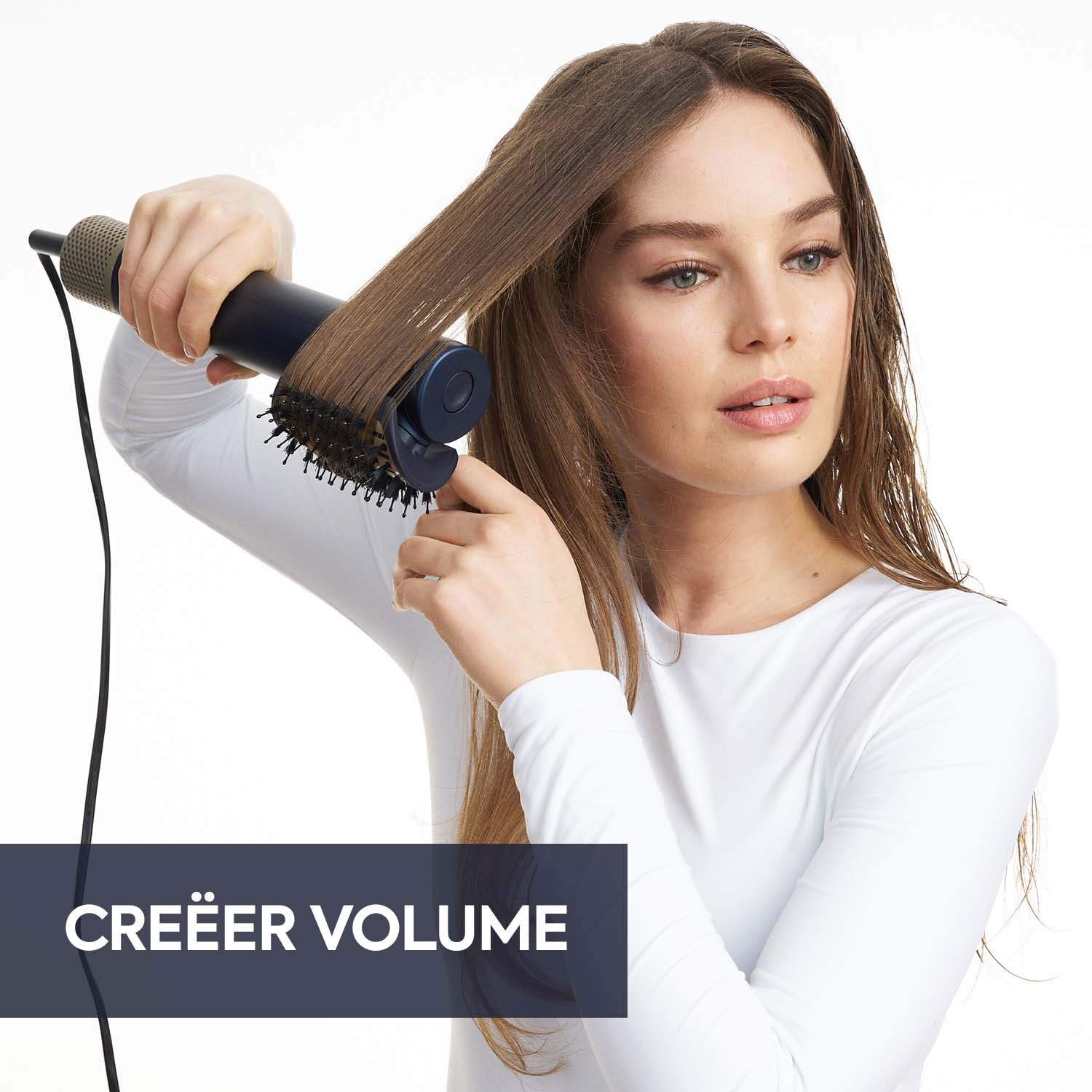 Vrouw gebruikt een haarstylingtool op haar haar. Ze draagt wit en kijkt naar de camera. Tekst: CREËER VOLUME.