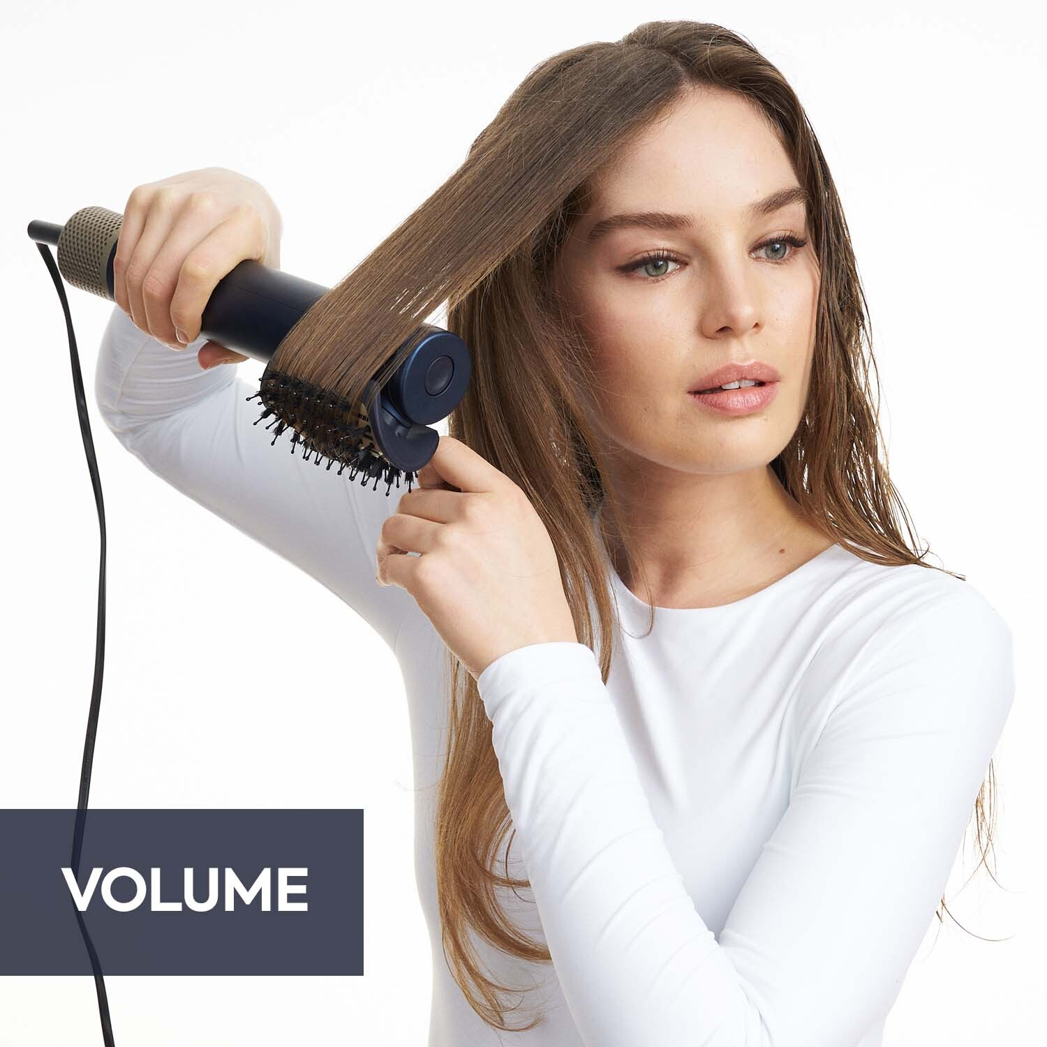 Femme se coiffant avec une brosse. Tient un outil de coiffage. Texte 'VOLUME' en bas à gauche.
