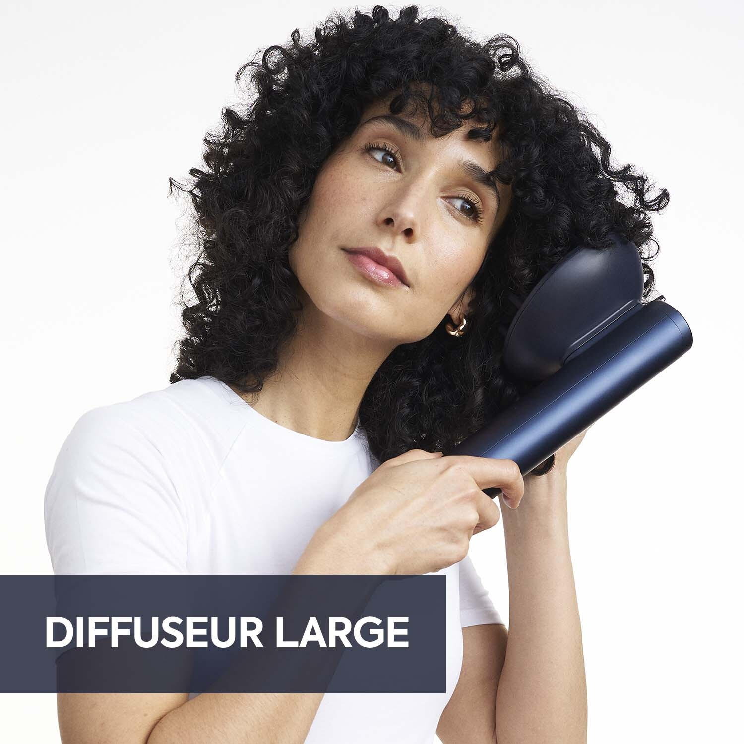Femme aux cheveux bouclés utilisant un diffuseur de cheveux bleu. Elle porte un t-shirt blanc. Le fond est blanc. Texte : DIFFUSEUR LARGE.