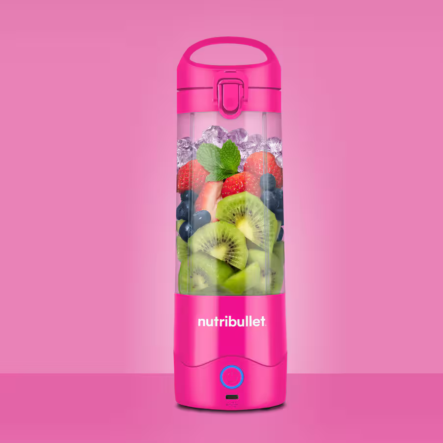 Różowy Nutribullet wypełniony kiwi, jagodami, truskawkami, lodem i miętą na różowym tle.