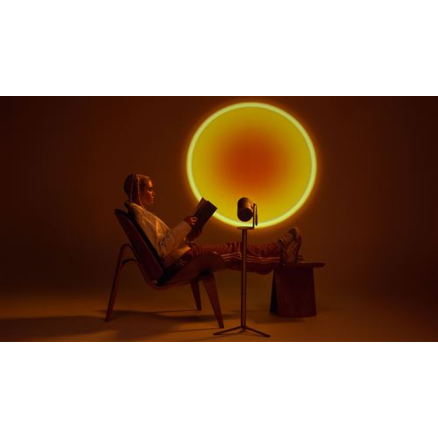 Vrouw leest boek, zit in stoel, benen op kleine tafel. Zonsonderganglamp verlicht de achtergrond.