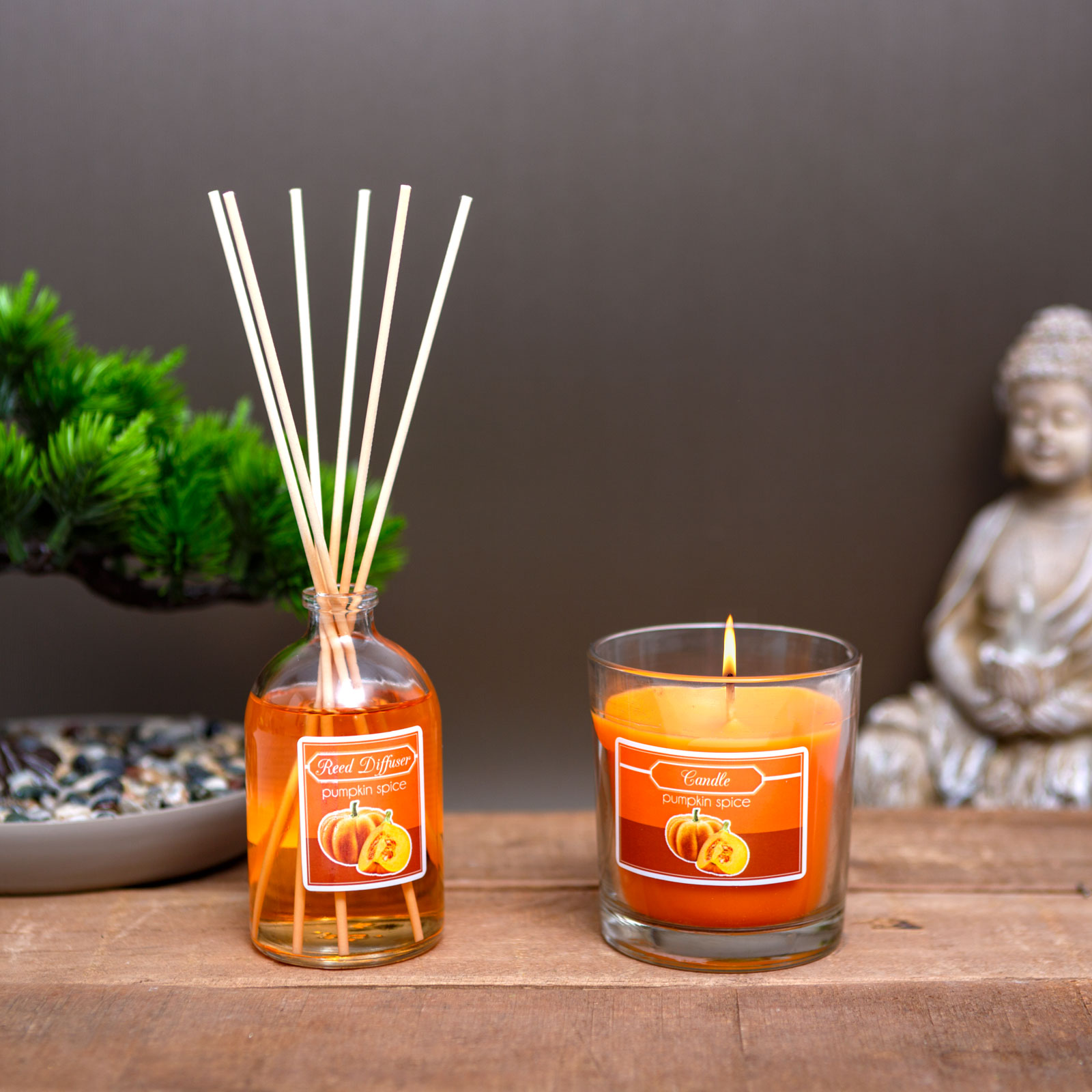 Egy narancssárga gyertya és egy 'Pumpkin Spice' feliratú illatpálca faanyagon. Hátul egy Buddha-szobor.