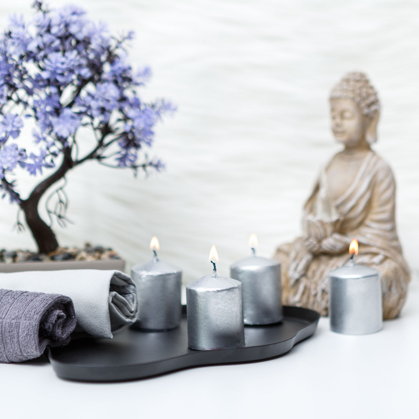Zen jelenet égő gyertyákkal, Buddha szoborral és bonsai-val. Puha törölközők és egy lila virágú fa a jelenetben.