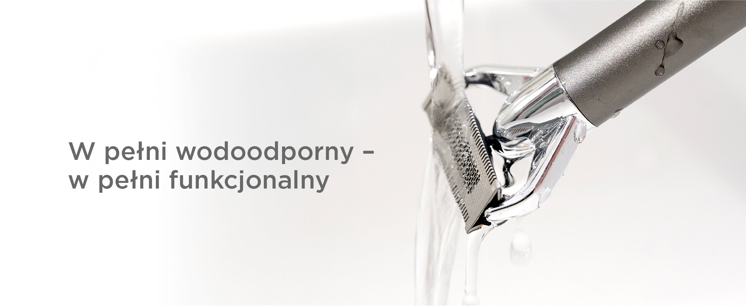 Zbliżenie metalowej maszynki do golenia pod bieżącą wodą. Woda spływa po ostrzu. Tekst: W pełni wodoodporny - w pełni funkcjonalny.