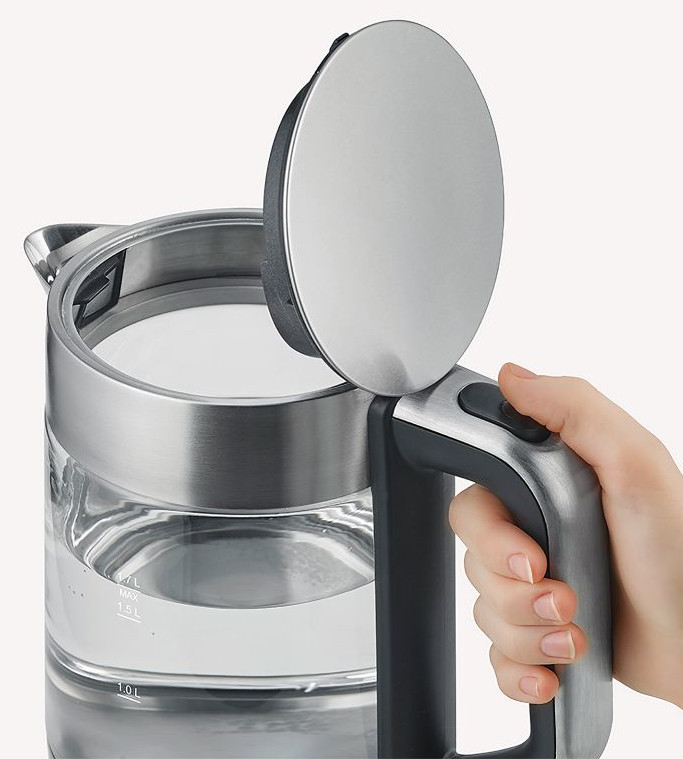 Ręka otwiera czajnik elektryczny ze stali nierdzewnej. Szklany czajnik zawiera wodę. Pokrywa jest otwarta, odsłaniając wnętrze.