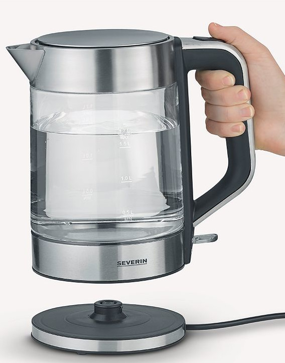 Szklany czajnik z wodą trzymany przez rękę. Znajduje się nad czarną podstawą z przewodem zasilającym.