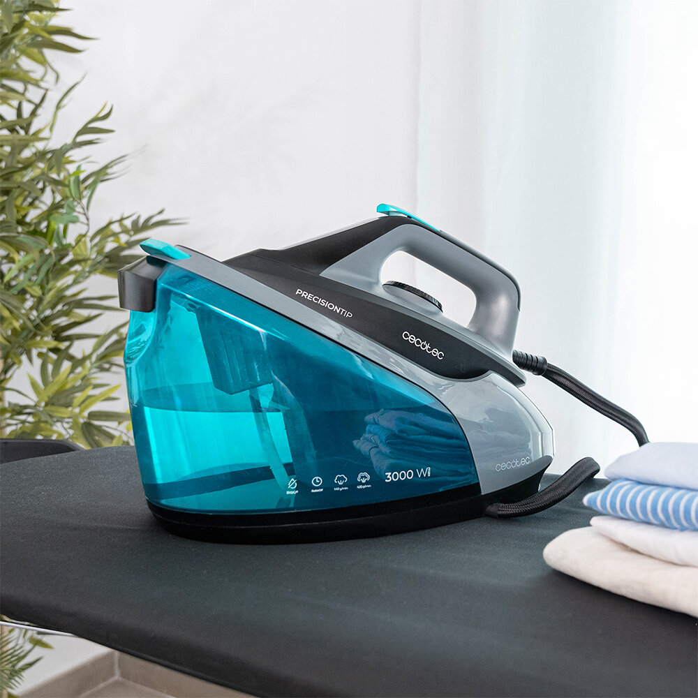 Niebiesko-czarne żelazko stoi na desce do prasowania obok złożonych ubrań. Zielona roślina i biała zasłona w tle.