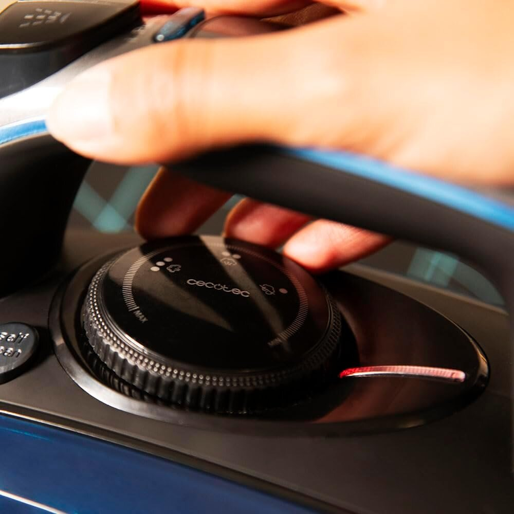 Ręka obraca czarne pokrętło na żelazku Cecotec. Pokrętło ma ustawienia i czerwone światło. Żelazko ma niebieskie i czarne akcenty.