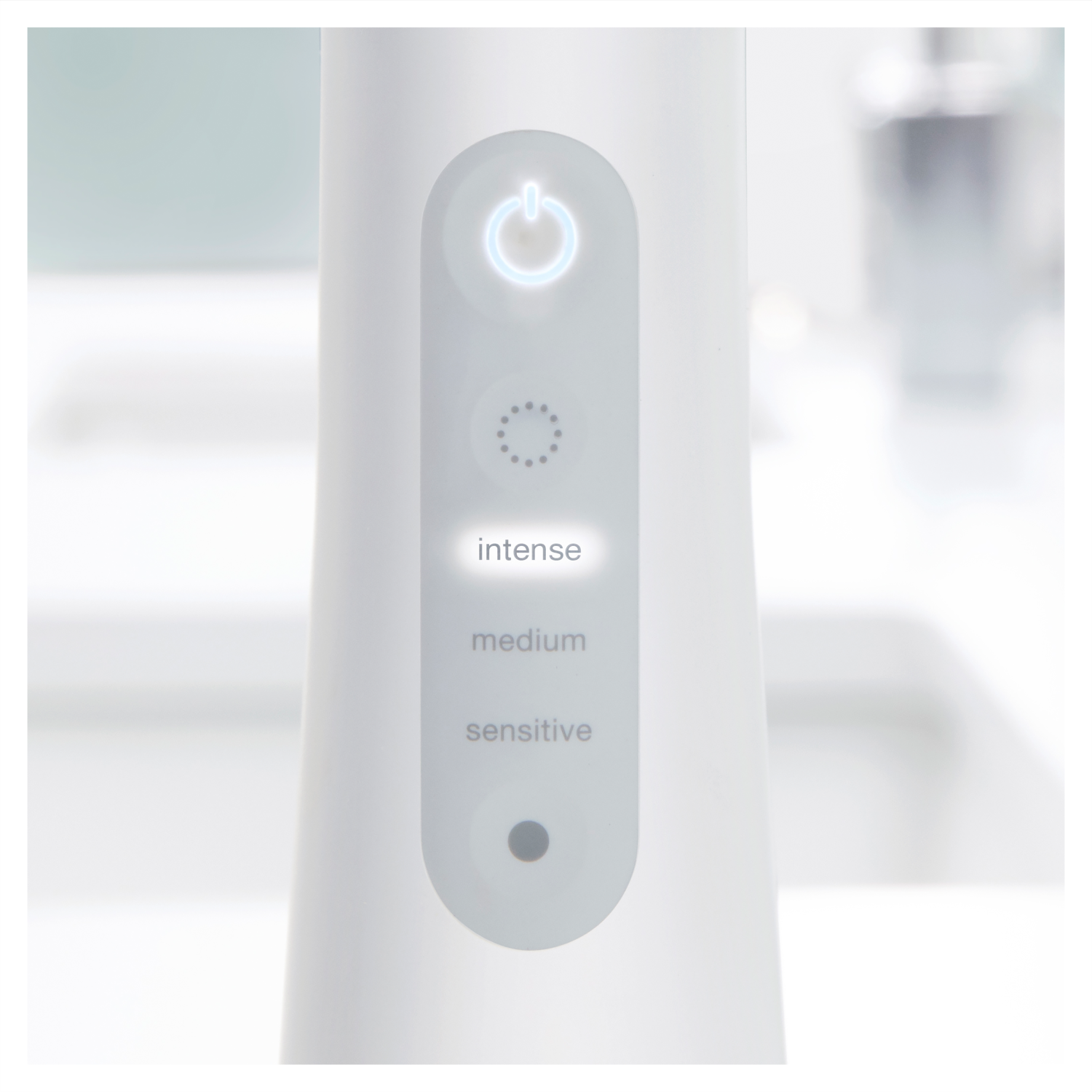 Biały panel sterowania urządzenia z podświetlanym przyciskiem zasilania i ustawieniami intensywności: intensywny, średni, wrażliwy.