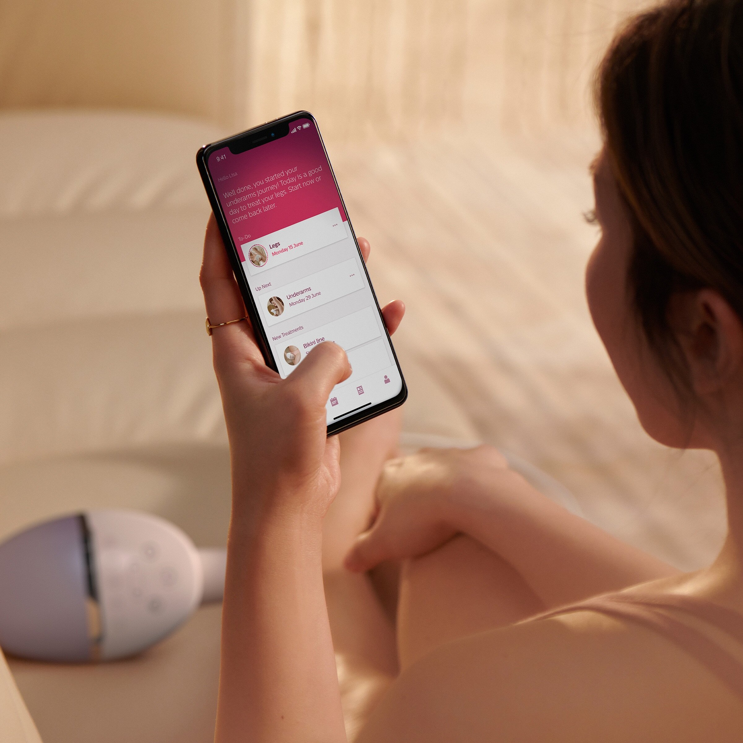 Kobieta trzyma telefon z aplikacją do leczenia. Urządzenie jest w tle. Scena ma różowawy odcień.