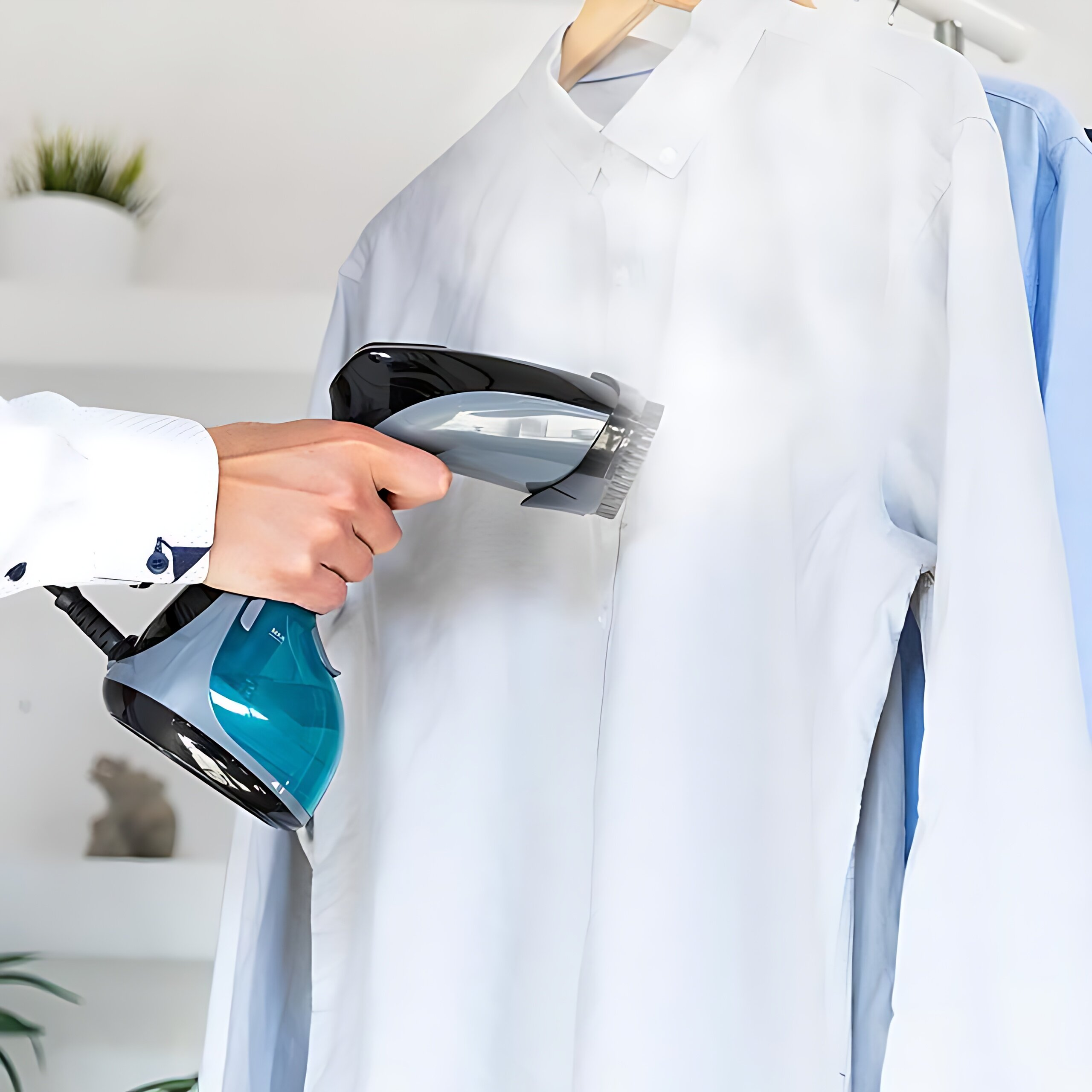 Osoba paruje białą koszulę parownicą ręczną. W tle wiszą inne koszule.