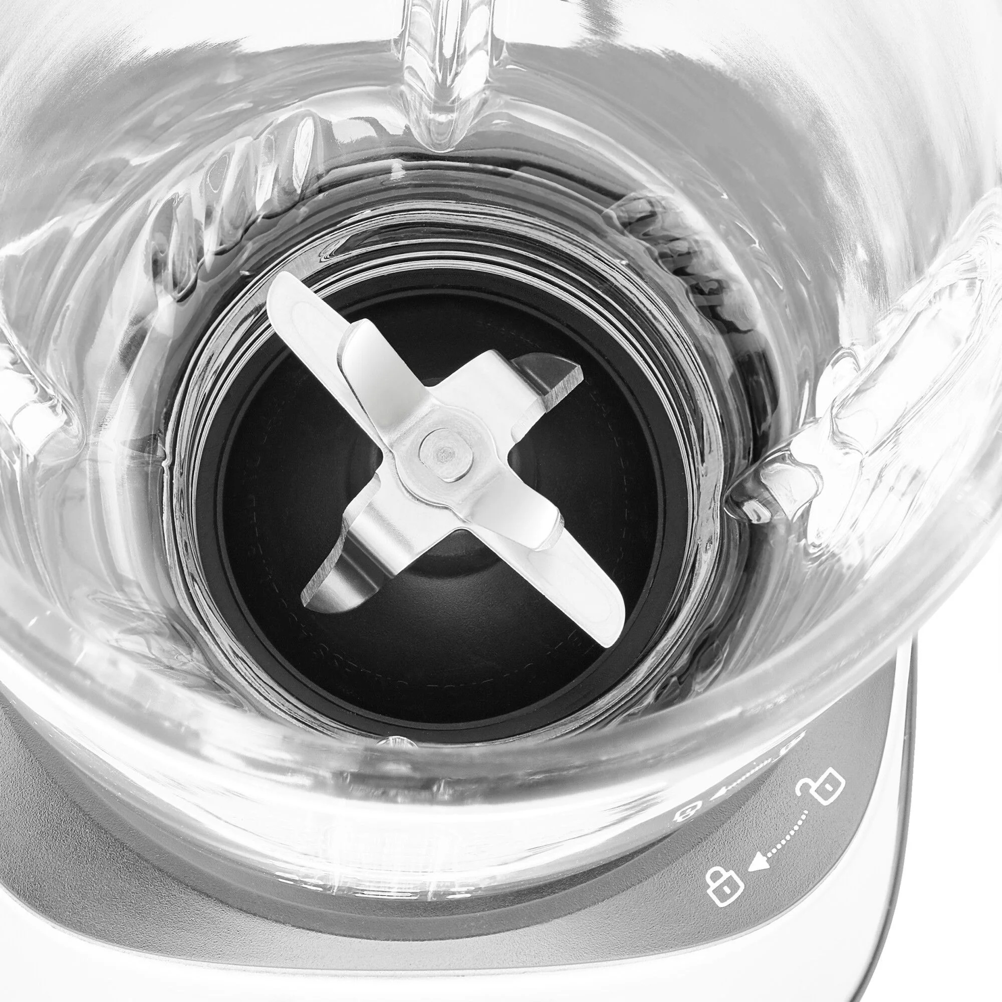 Zbliżenie blendera. Srebrne ostrze znajduje się w środku szklanego pojemnika. Podstawa jest szara.