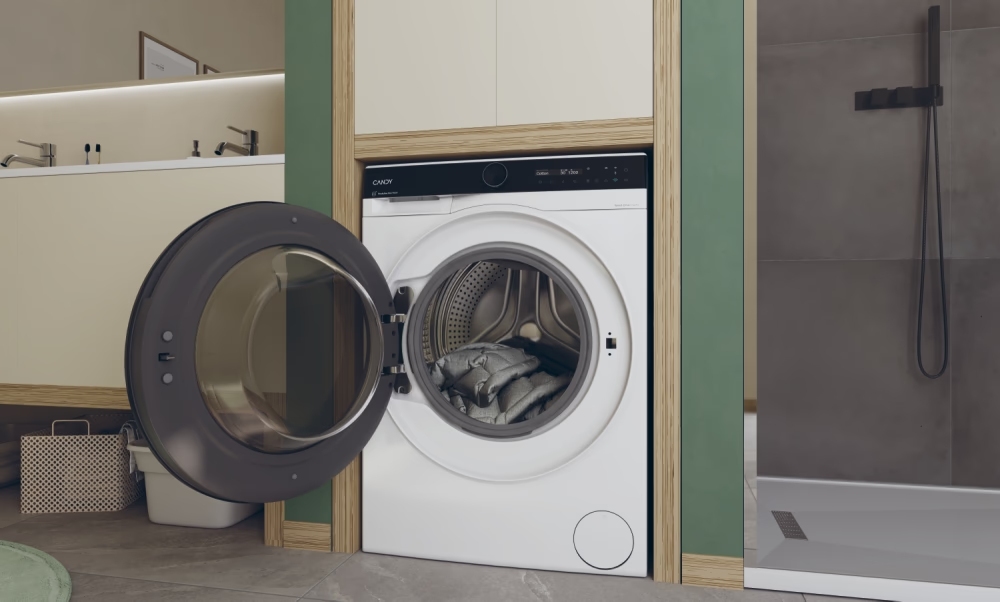 Waschmaschine mit offener Tür, Kleidung im Inneren. Waschraum mit grüner Wand und Dusche.