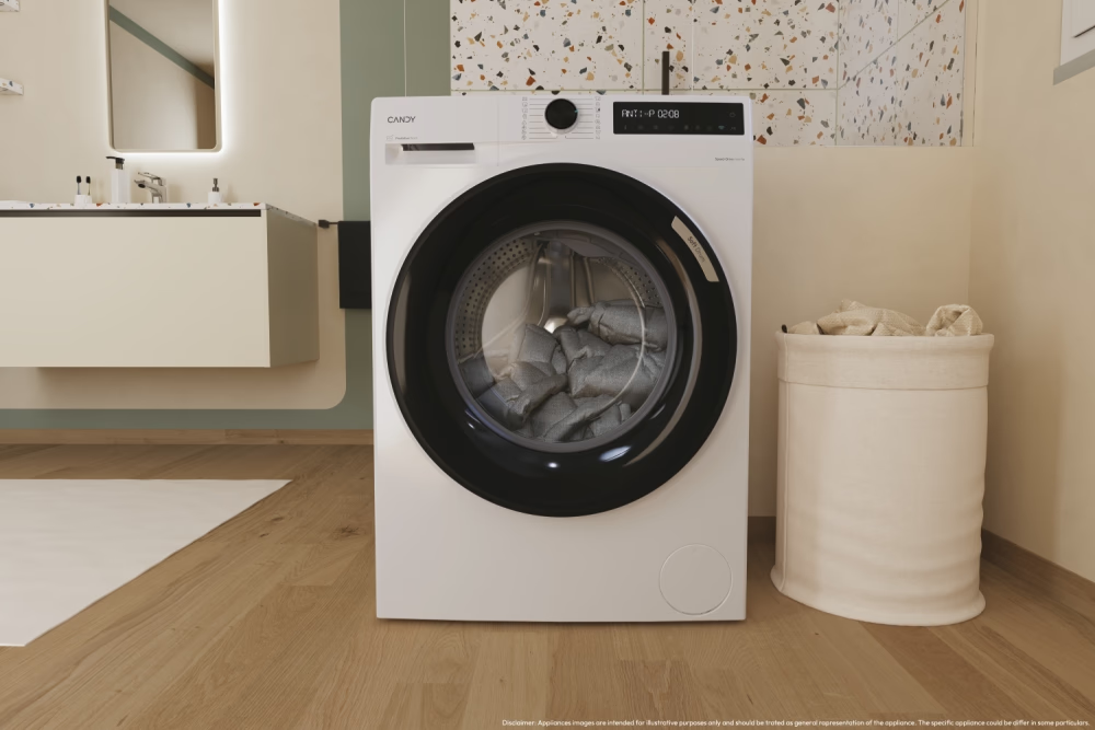 Una lavatrice bianca con porta nera è in un bagno. Un cesto per la biancheria è a destra.