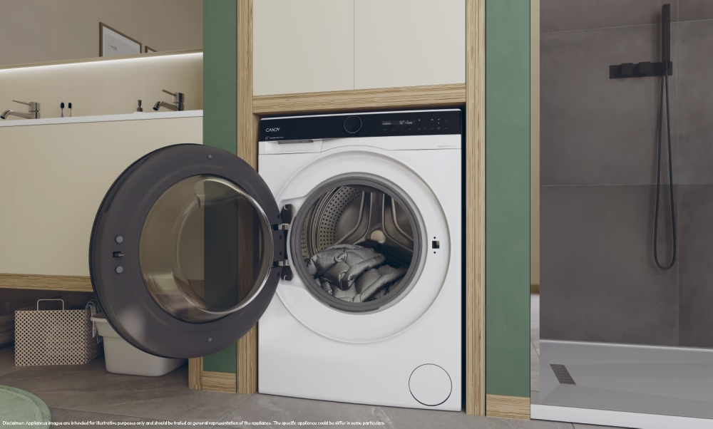 Eine Waschmaschine mit offener Tür, die Kleidung im Inneren zeigt. Der Hintergrund zeigt ein Badezimmer mit Dusche und Waschbereich.