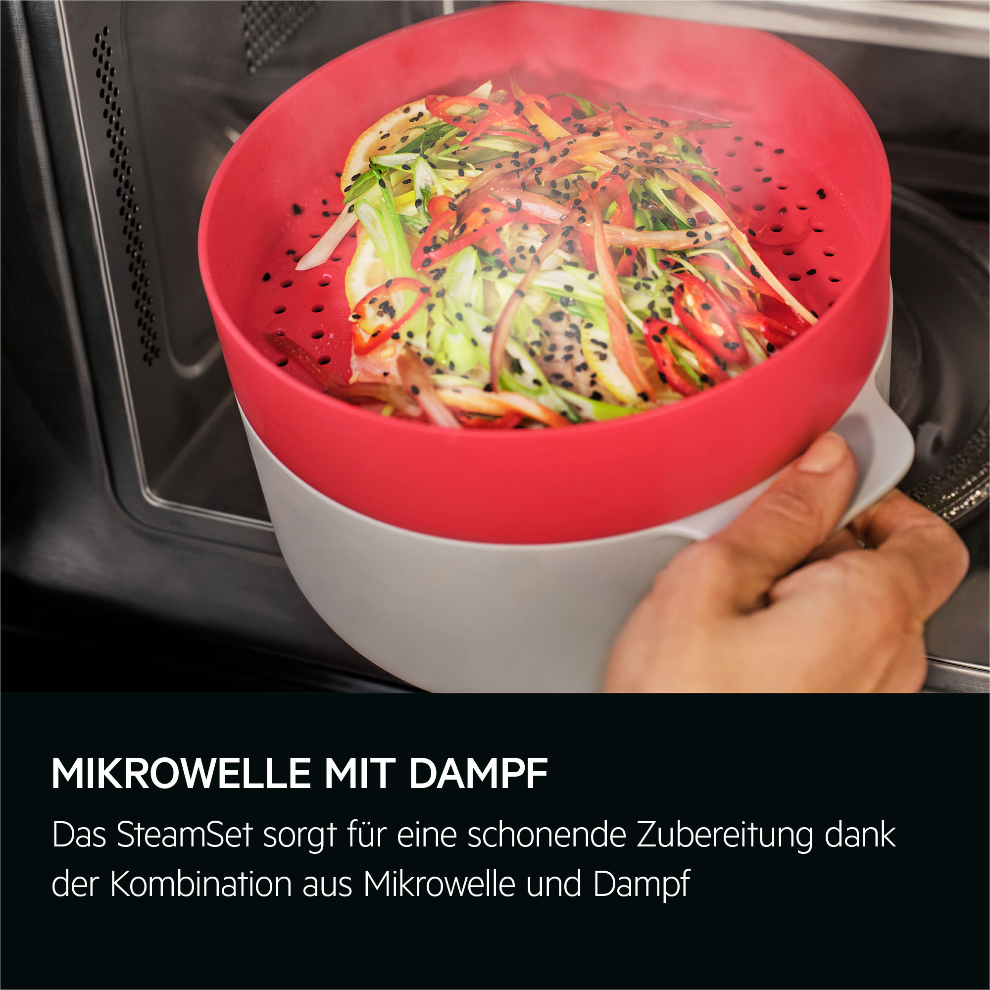 Ein roter Dampfgarer mit Gemüse wird von einer Hand gehalten. Dampf steigt auf. Der Hintergrund ist eine Mikrowelle.