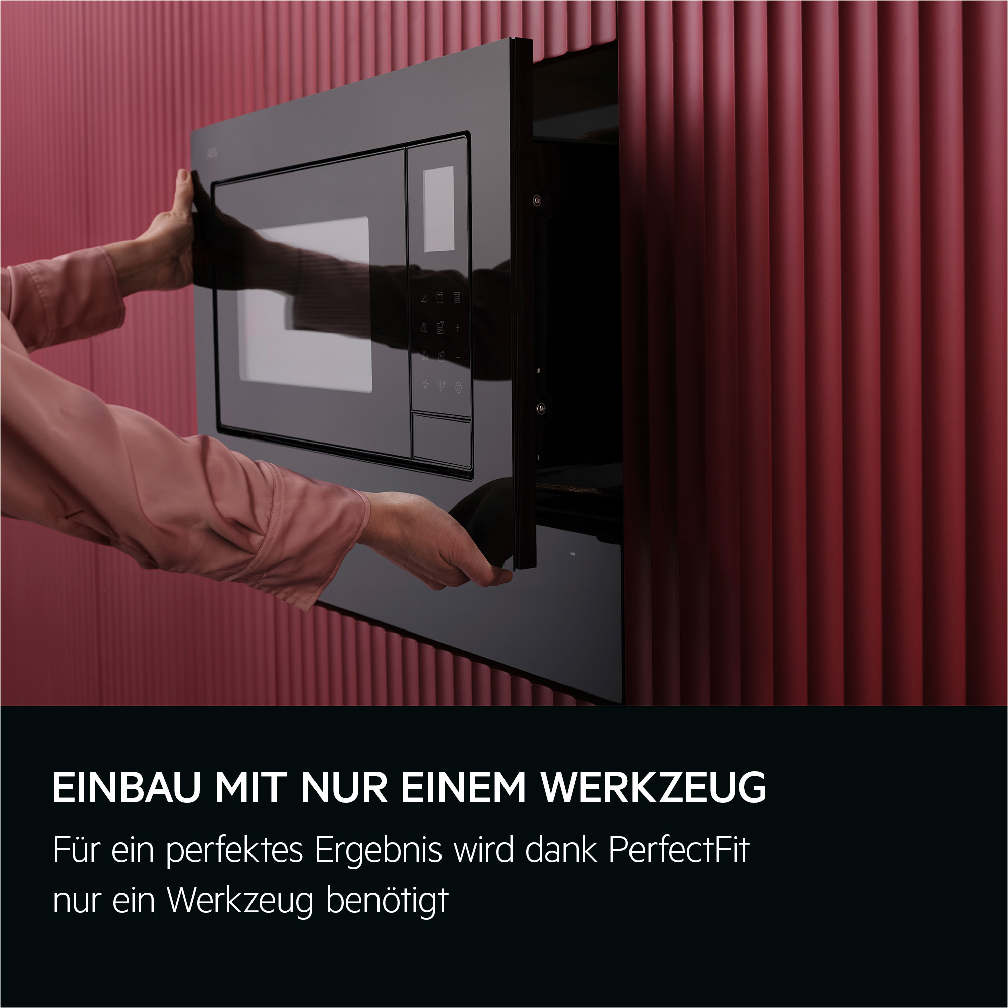 Eine Person installiert eine schwarze Mikrowelle in eine Wand. Der Hintergrund ist eine burgunderfarbene strukturierte Wand.