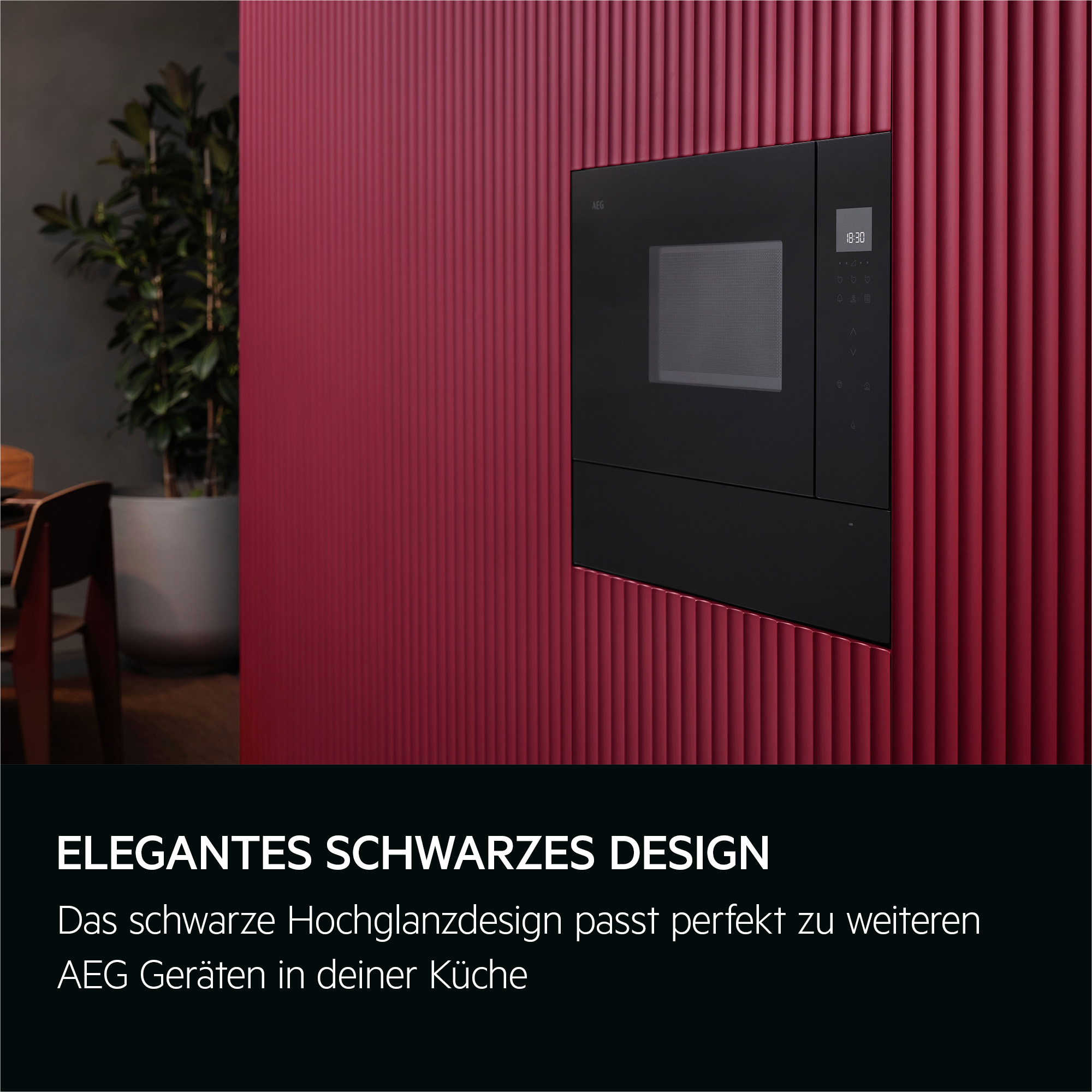 Eine schwarze Mikrowelle ist an einer roten Wand montiert. Eine grüne Pflanze und ein Esstisch sind im Hintergrund sichtbar.