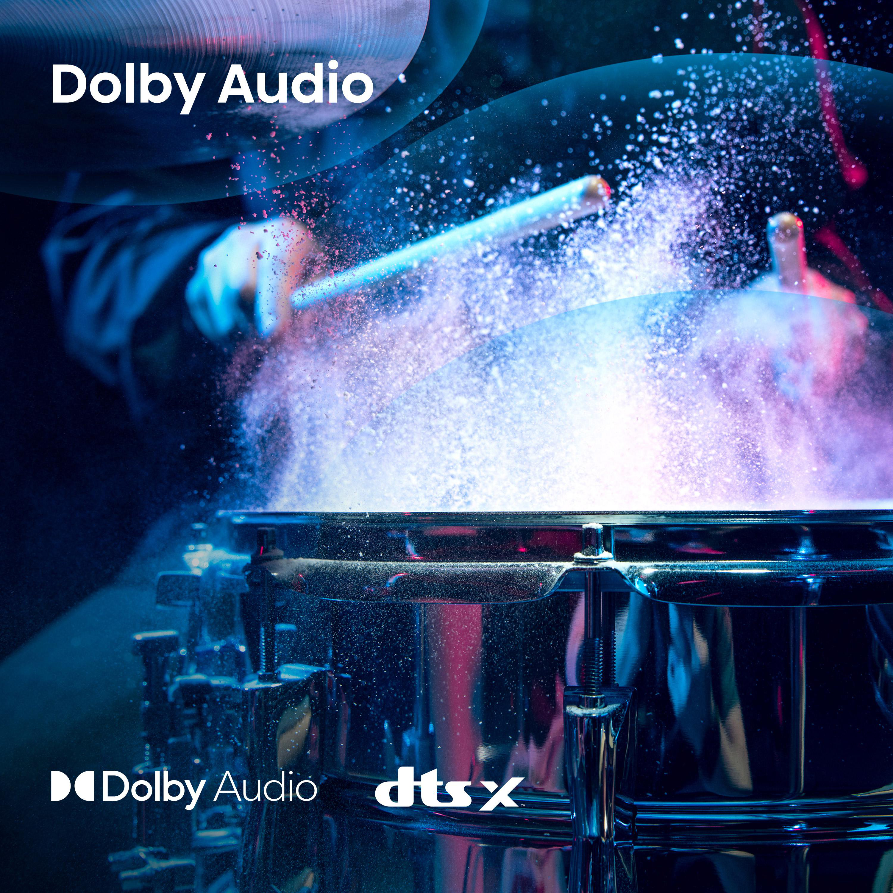Schlagzeuger schlägt auf eine Trommel. Farbige Pulverexplosion. Dolby Audio und DTS:X Logos vorhanden.