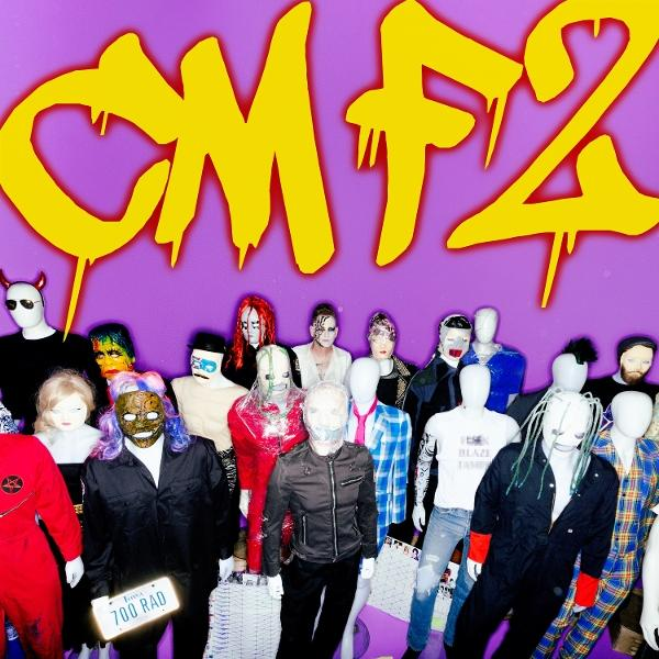 Groupe de figures masquées sous lettres jaunes "CMF2" sur fond violet. Certaines portent des costumes ou des masques.
